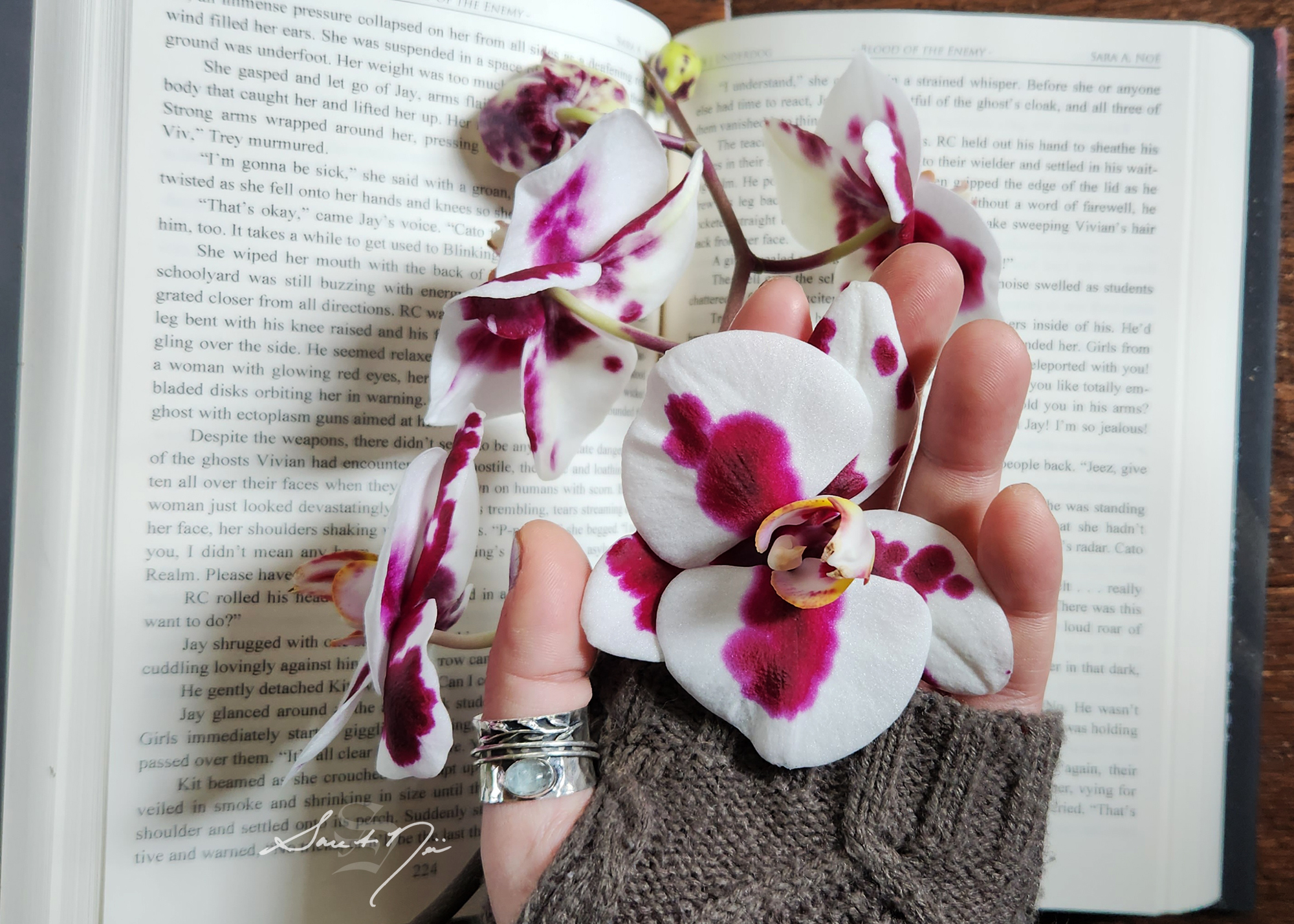 Hand holding an orchid in front of an open book
